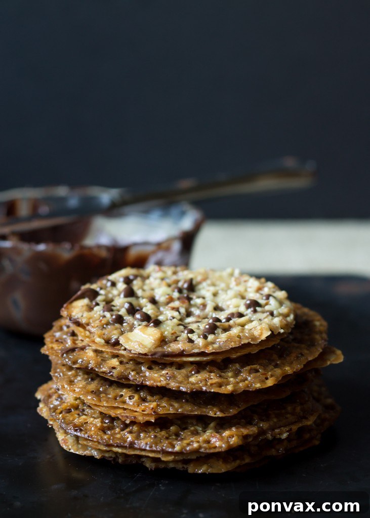 A close-up of crispy homemade Dark Chocolate Almond Lacey Cookies, with a generous layer of dark chocolate nestled between two delicate almond wafers.
