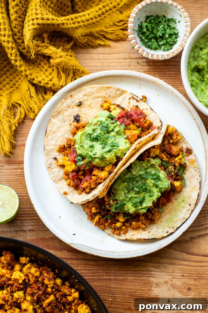 Two vegan breakfast tacos with tofu scramble and soy chorizo, topped with salsa, guacamole, and cilantro.