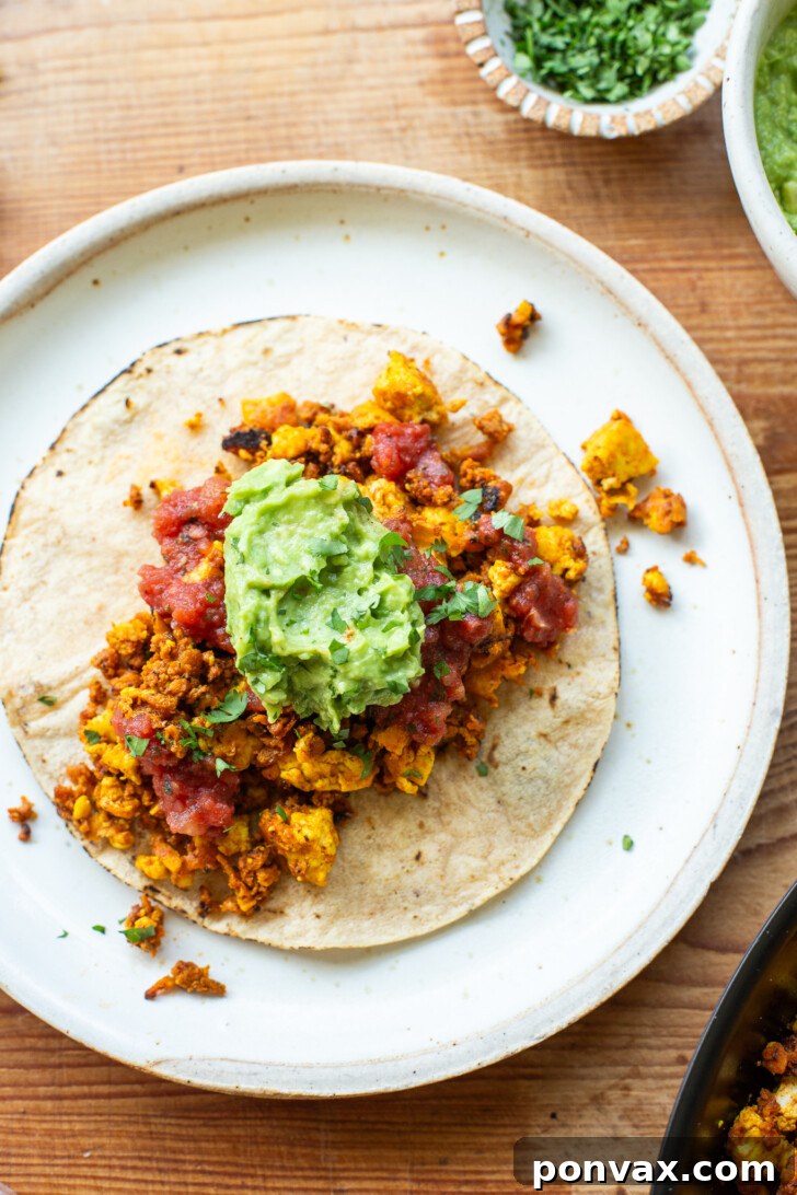 Three vegan breakfast tacos arranged on a plate, showcasing the tofu scramble, soy chorizo, salsa, and avocado toppings.