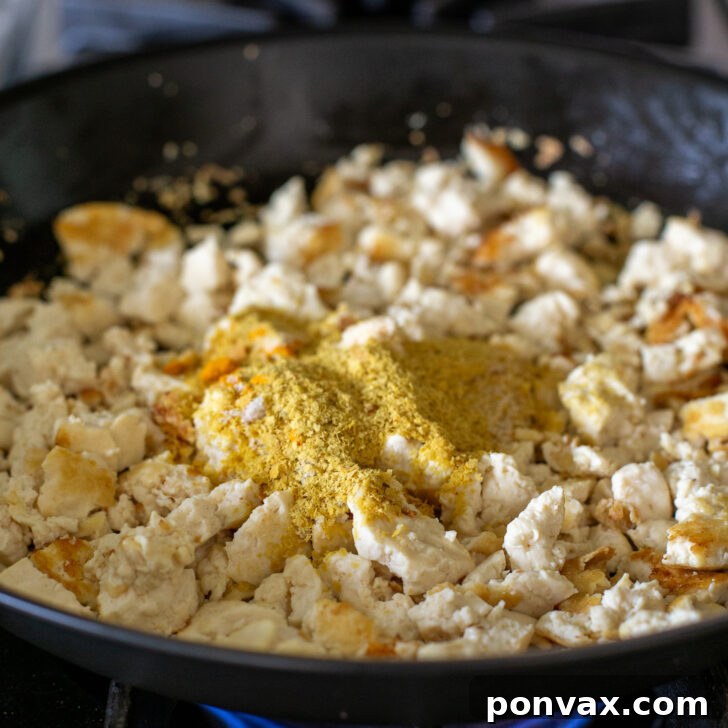 Step 3: Adding spices like nutritional yeast and turmeric to the sautéed tofu.