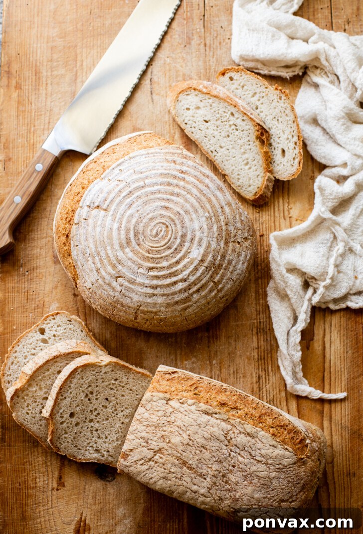 A perfectly baked, crusty gluten-free bread loaf with a slight tang from yogurt, sliced to reveal its soft, airy interior. This loaf is considered the best gluten-free bread ever, offering a sourdough-like flavor without a starter.
