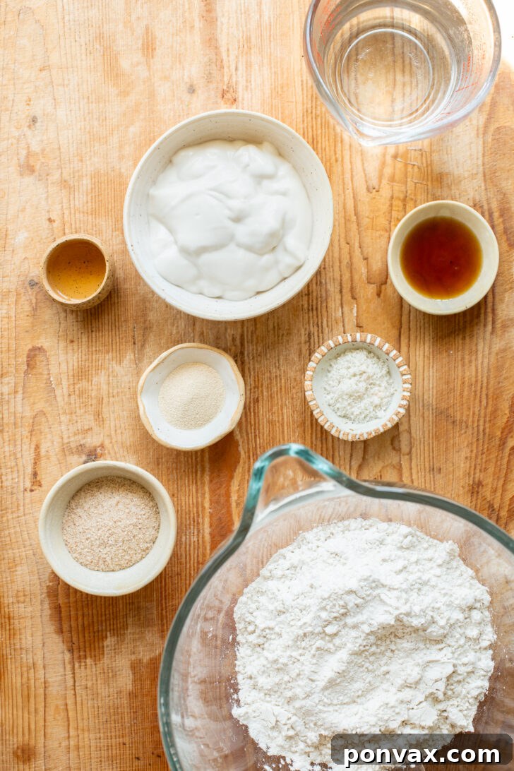 A collection of the seven essential ingredients for making gluten-free yogurt bread, including psyllium husk, gluten-free flour blend, yogurt, and yeast, arranged neatly on a counter.