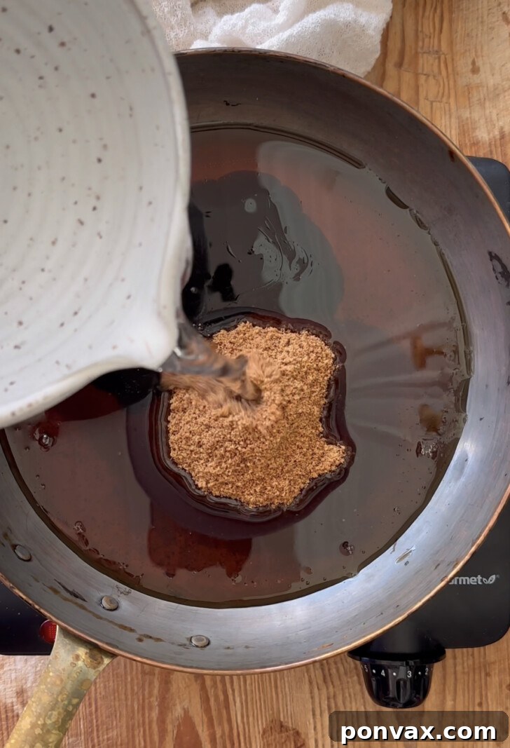 Handcrafted Gingerbread Elixir 4 Maple syrup being poured into a saucepan with water and coconut sugar for homemade gingerbread syrup.