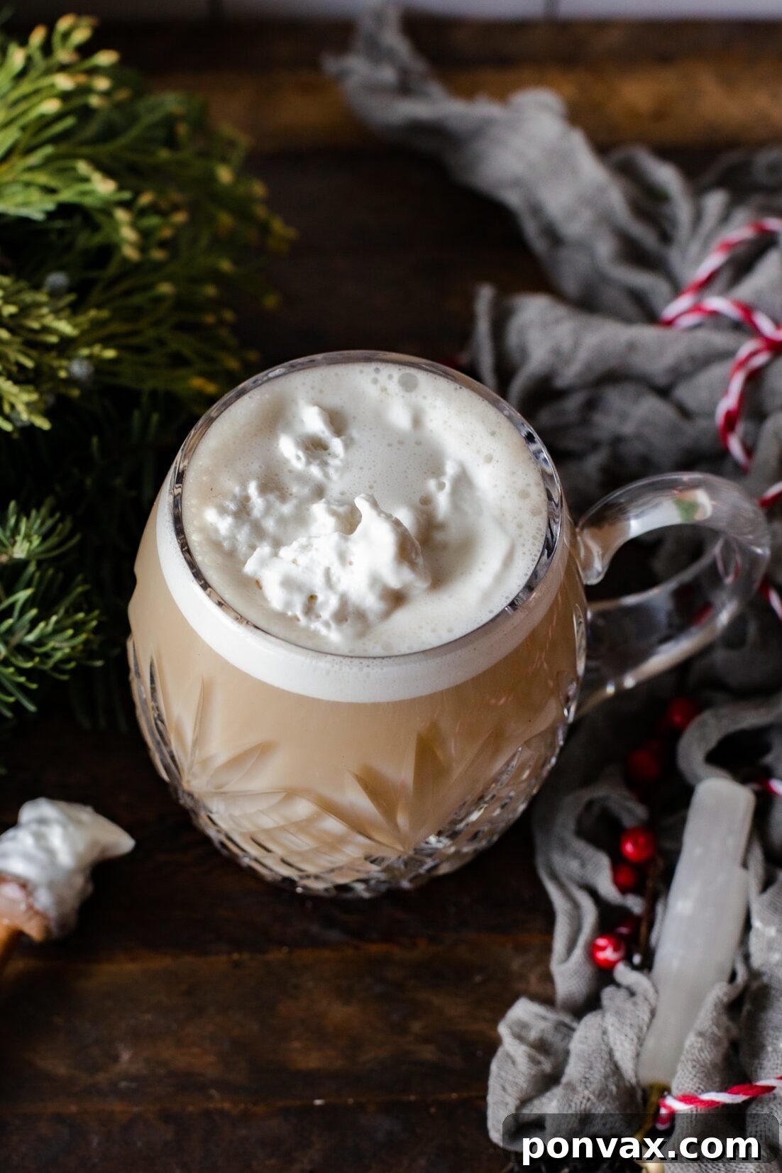 A beautifully presented London Fog Tea Latte in a clear mug, topped with frothed milk and a hint of steam rising, placed on a rustic wooden surface next to tea bags and a small bowl of maple syrup.