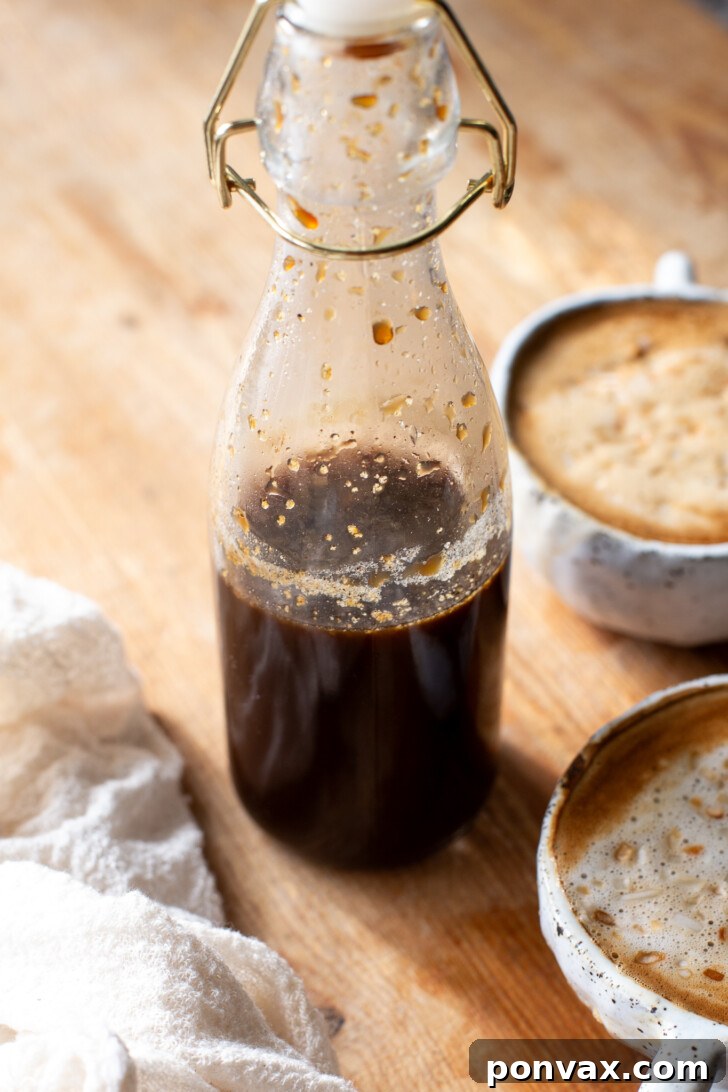 Tropical Coconut Elixir 8 A beautifully frothed homemade coconut latte with a decorative sprinkle on top, served with a bottle of coconut syrup and a small bowl of coconut flakes.