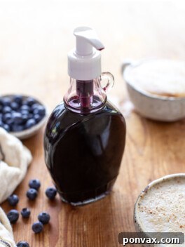 Sweet Blueberry Elixir: Elevate Your Lattes, Cocktails, and Culinary Creations 5 A glass bottle of homemade blueberry syrup on a wood board with a blueberry oat milk latte in front and a bowl of blueberries on the side.