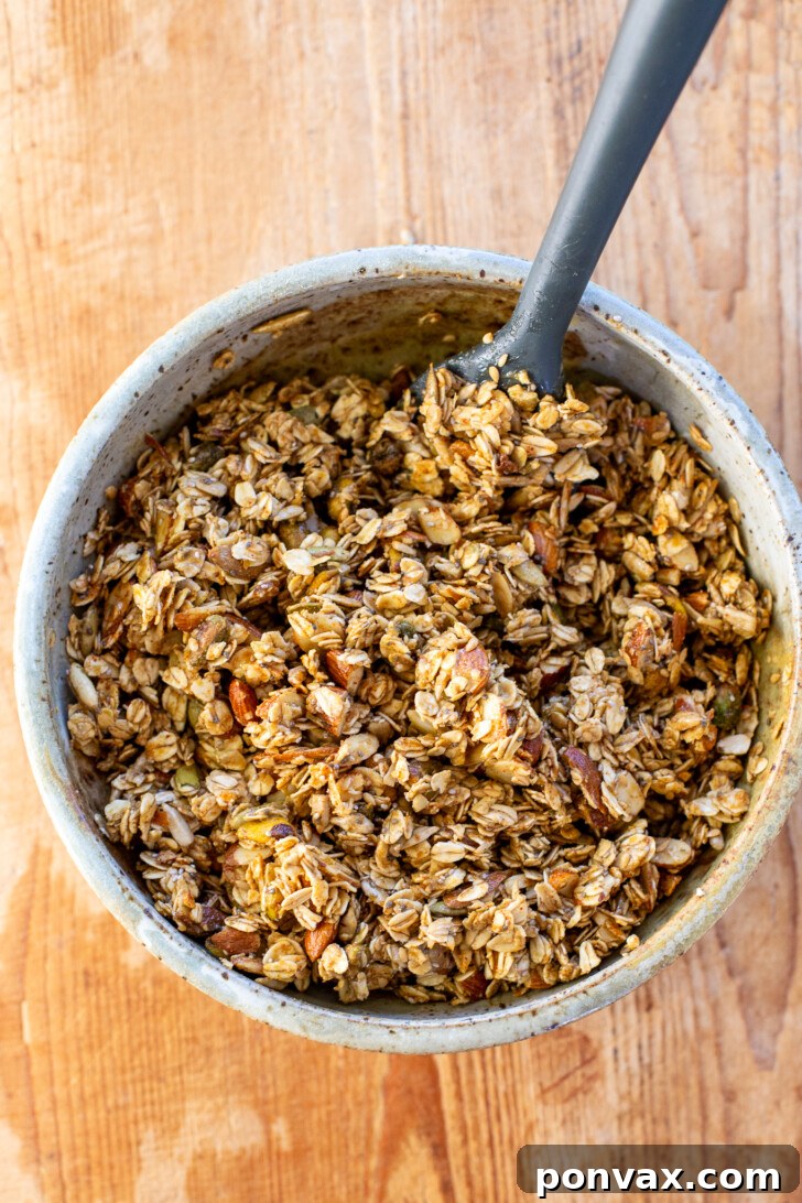 Savory granola spread on a parchment-lined baking sheet before baking.