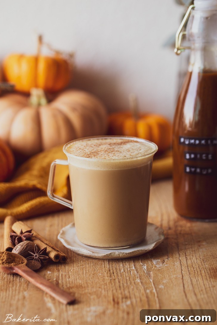A latte being poured into a mug, creating a beautiful swirl of coffee and frothed milk. The setting evokes a cozy autumn atmosphere.