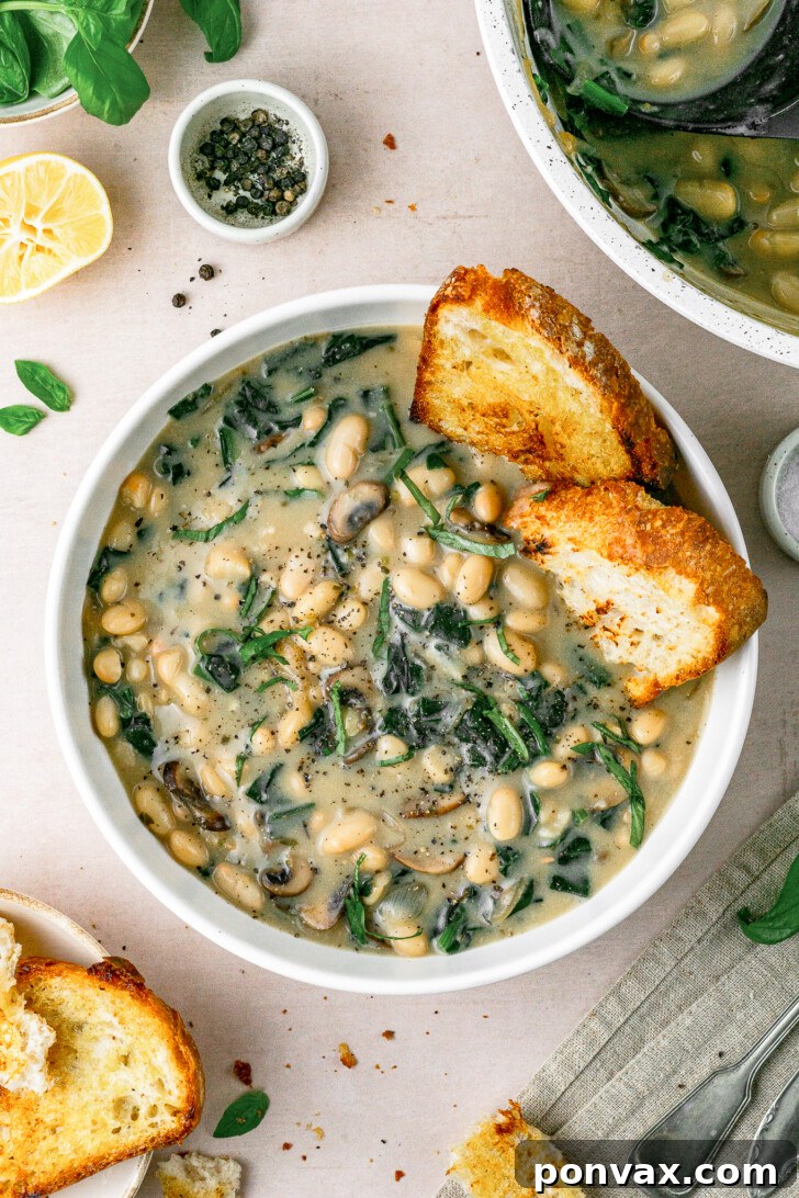 Wholesome One-Pot White Bean Mushroom Stew 2 A beautiful bowl of creamy vegan white bean mushroom stew, garnished with fresh basil, and served with a side of crispy sourdough bread for dipping.