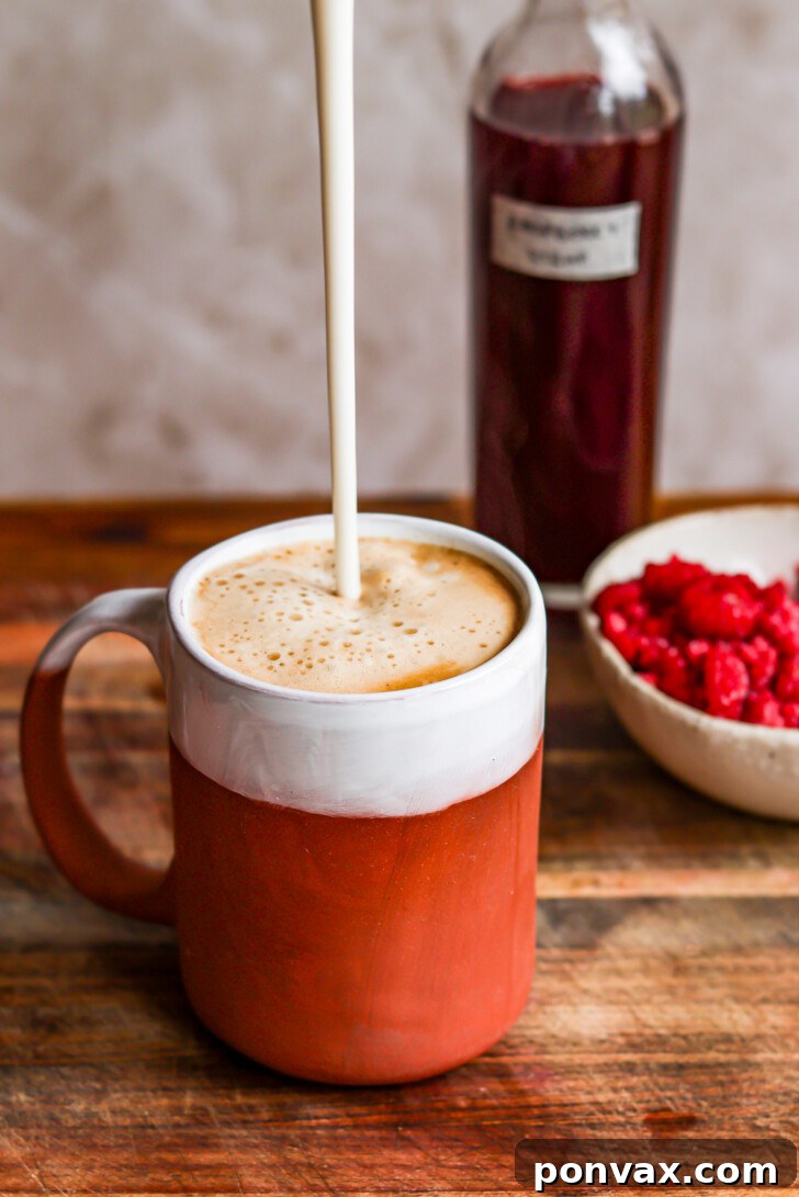 Homemade raspberry syrup served in a glass alongside a refreshing drink, possibly sparkling water with lemon and mint, highlighting its use in beverages.