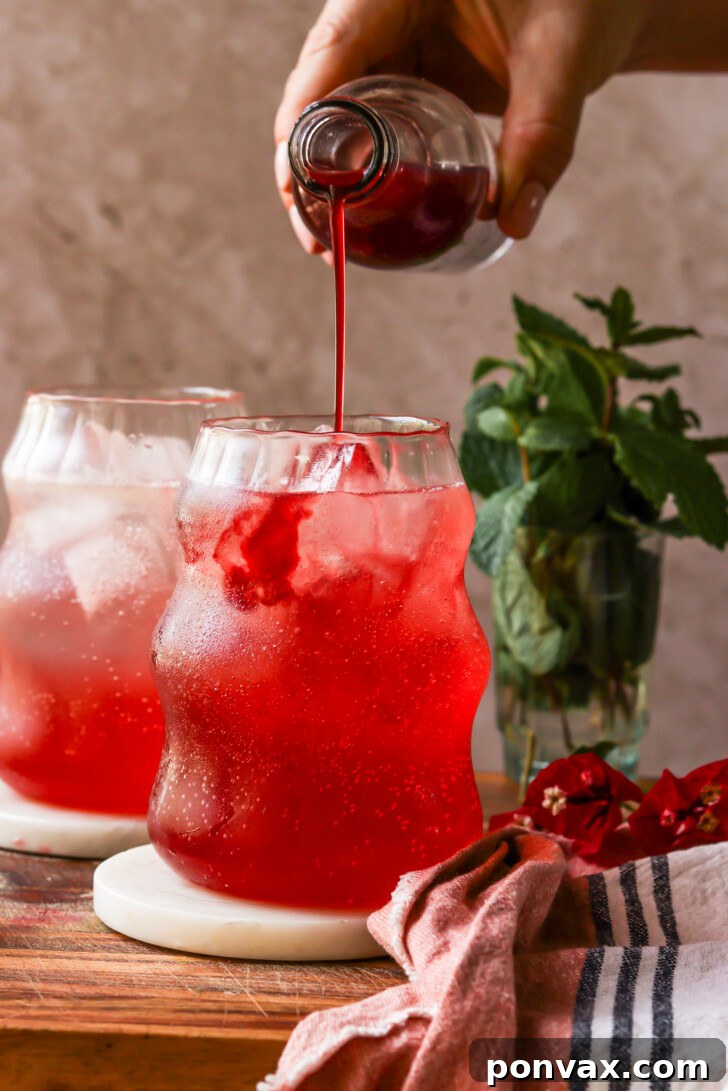 A close-up of a sparkling drink garnished with fresh raspberries and mint, showcasing the beautiful color and refreshing appeal created by the raspberry syrup.