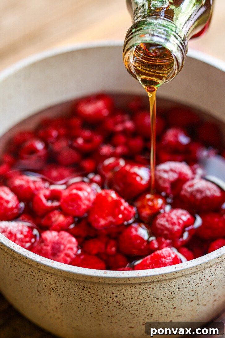 The raspberry mixture simmering gently in a saucepan, with berries starting to break down and release their color into the water.
