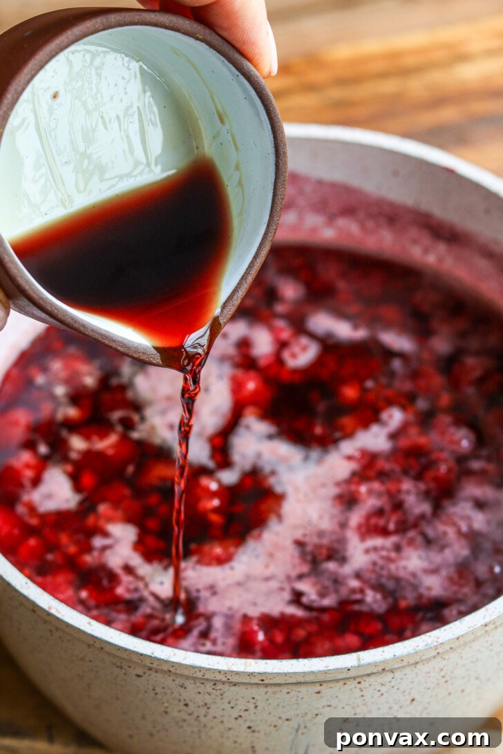Straining the simmered raspberry mixture through a fine-mesh sieve into a bowl, showing the smooth liquid separating from the pulp.