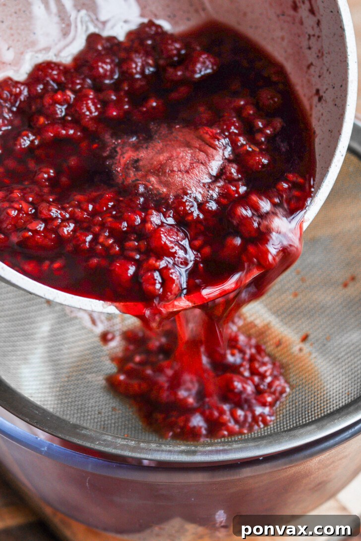 A closer view of the raspberry pulp being gently pressed against the sieve with a spoon to extract all remaining liquid, ensuring maximum flavor.