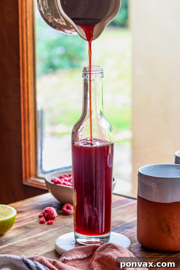 A beautifully bottled homemade raspberry syrup, ready for storage, with fresh raspberries scattered around, emphasizing its natural origin.