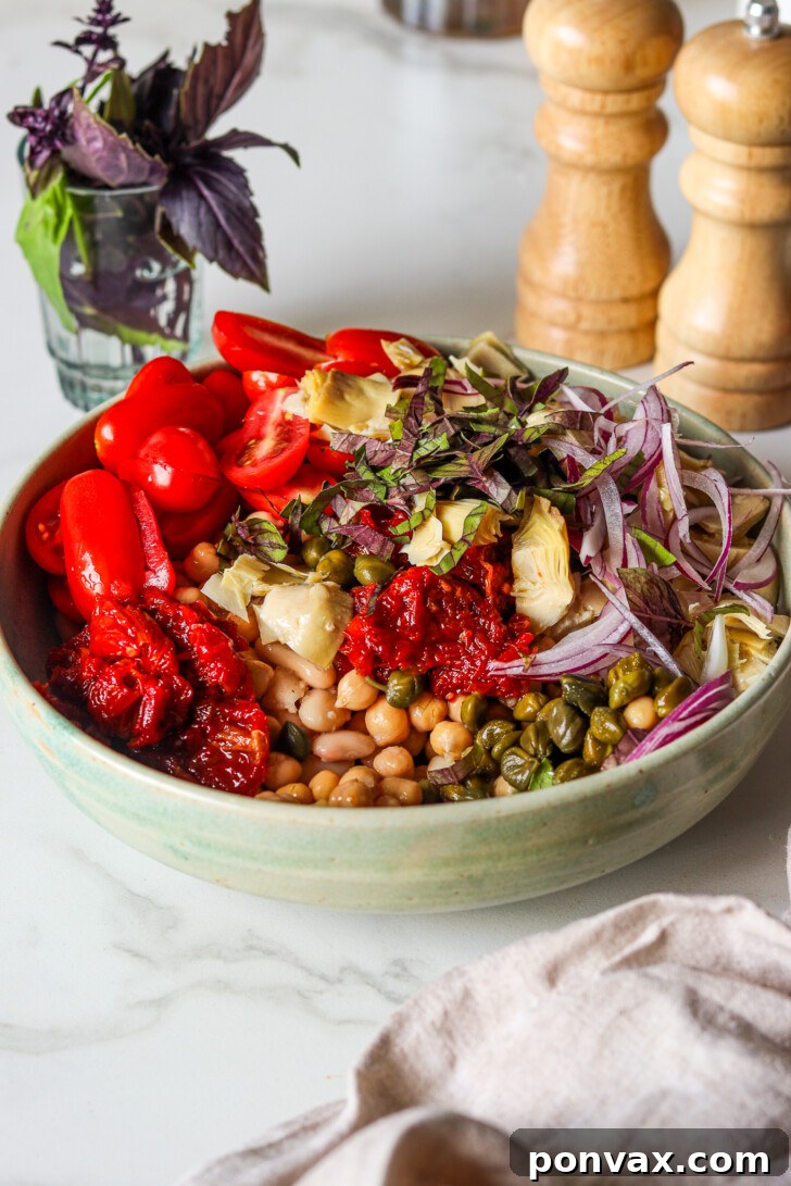 Mediterranean bean salad with white beans, chickpeas, capers, and artichoke hearts in a bowl.