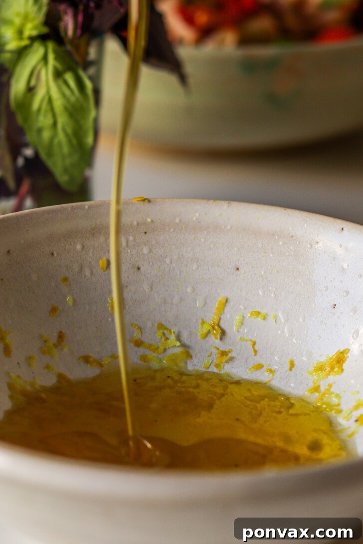 Olive oil being drizzled into a ceramic bowl with lemon zest to make a mediterranean-style dressing.