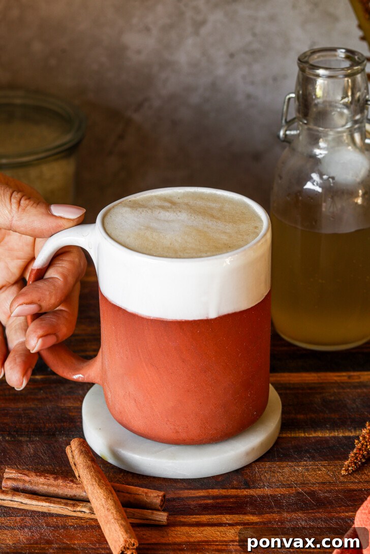 A glass of iced horchata latte with oat milk, garnished with a cinnamon stick.