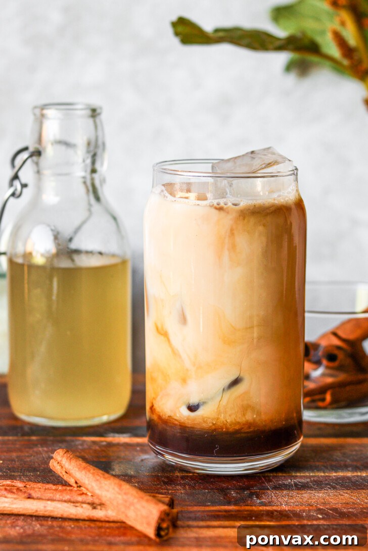 DIY Horchata Oatmilk Shaken Espresso Starbucks Style 5 A glass of Horchata Oatmilk Shaken Espresso with a bottle of homemade horchata syrup and cinnamon sticks on a rustic wooden board.