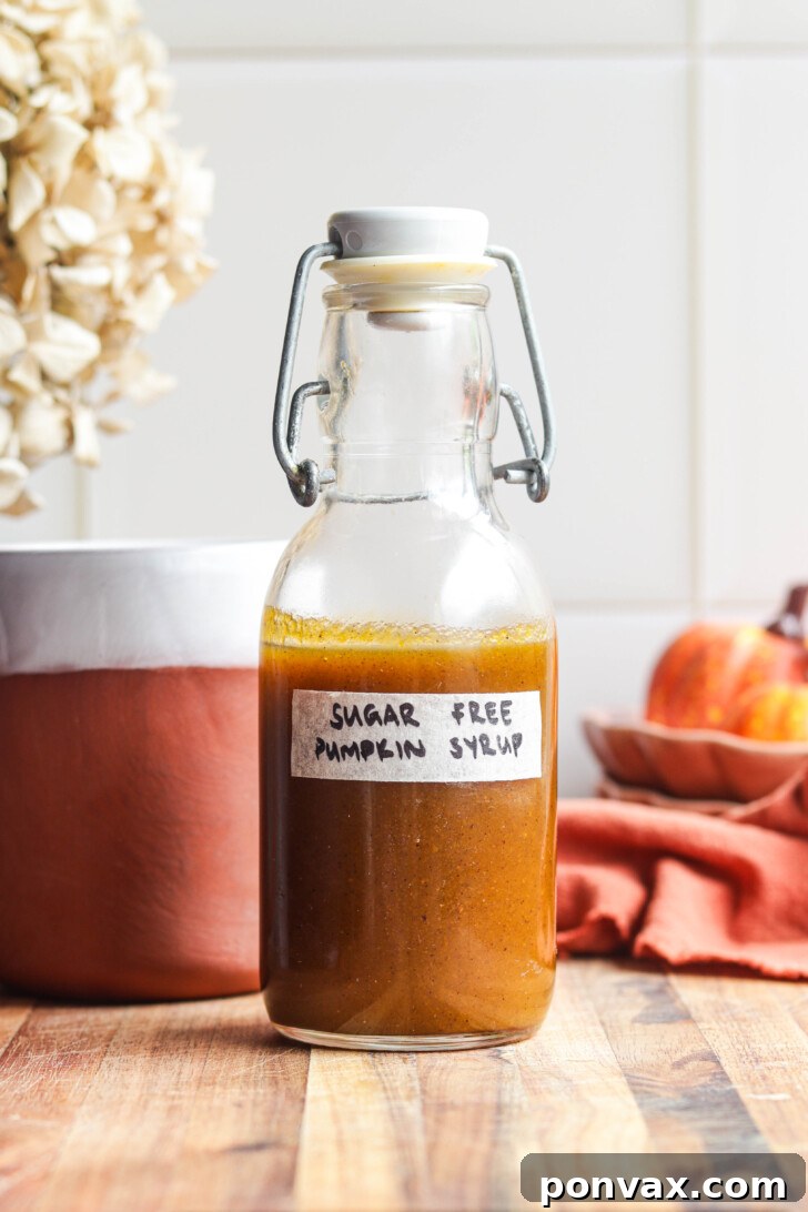 A glass bottle of homemade sugar-free pumpkin spice syrup, surrounded by fresh pumpkins and spices, evoking cozy fall vibes.