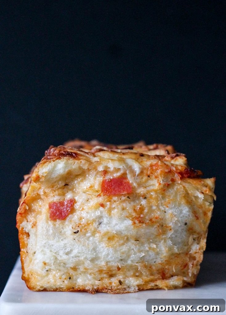 A top-down view of Pepperoni Pizza Pull Apart Bread in a loaf pan, with golden-brown crust and melted cheese visible between the slices, ready to be pulled apart.