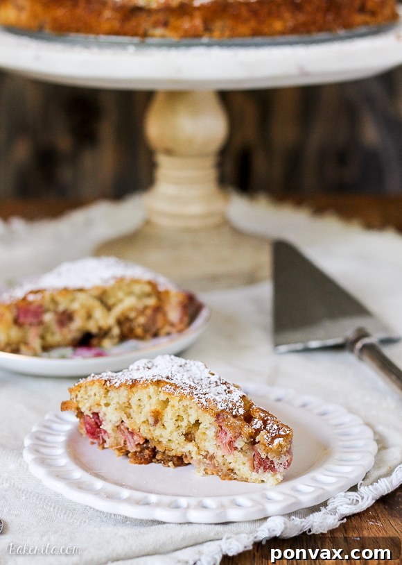 A beautifully presented Caramel Rhubarb Cake, showing a golden brown crust, visible ruby-red rhubarb pieces, and a rich, glistening caramel swirl on top. The cake sits on a rustic wooden surface, suggesting a homemade, comforting dessert ready to be enjoyed.