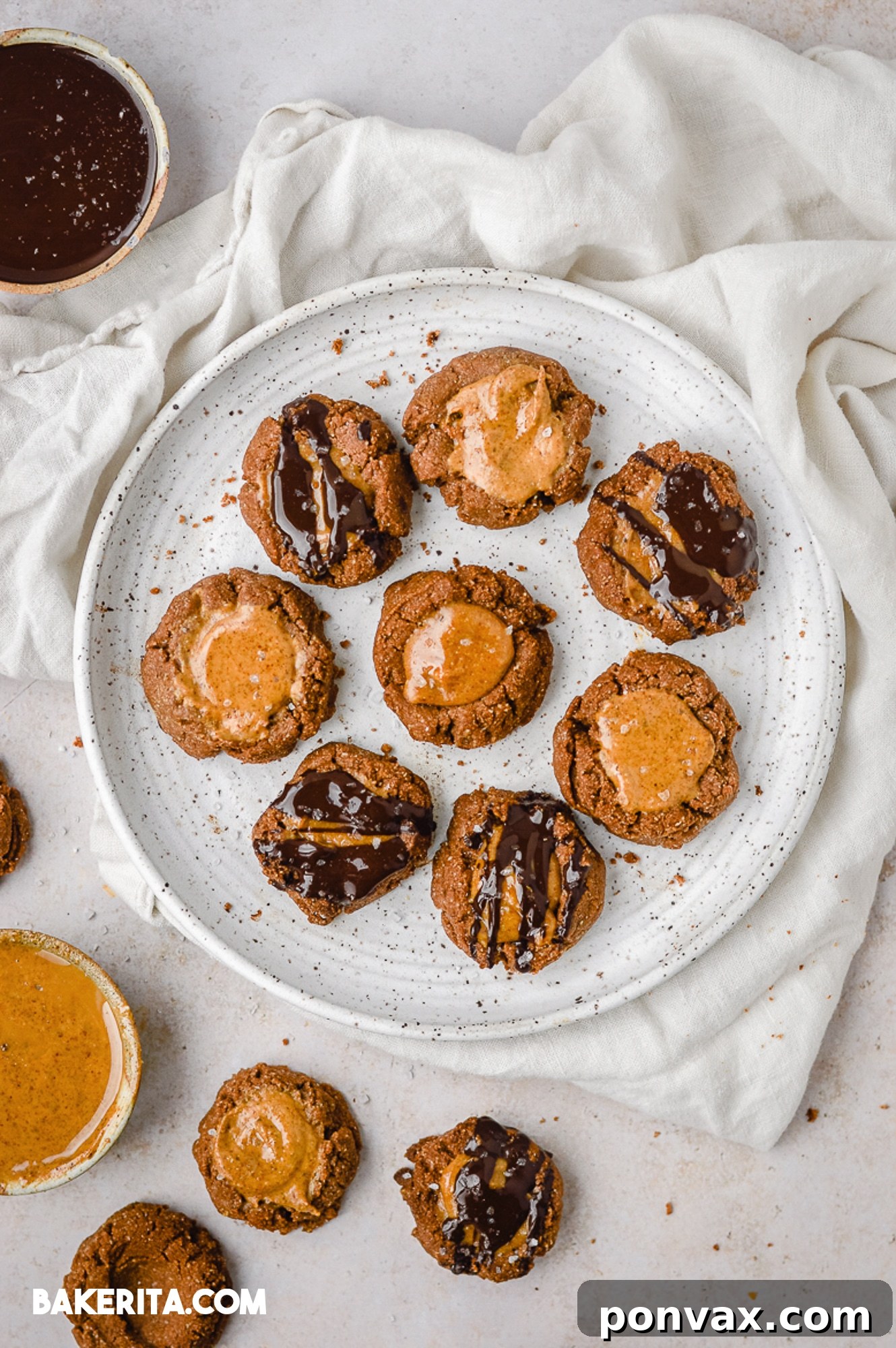 A plate of finished chocolate almond butter thumbprint cookies, drizzled with dark chocolate.