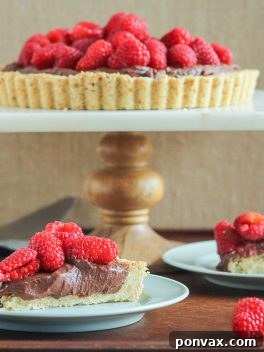 A detailed overhead shot of the finished Whipped Chocolate Ganache Raspberry Tart, garnished with an abundance of vibrant fresh raspberries, ready to be served.