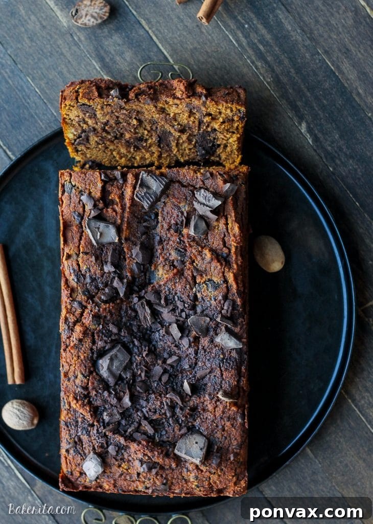 A large slice of Paleo Chocolate Chip Pumpkin Bread resting on a wooden board, showcasing its rich texture.