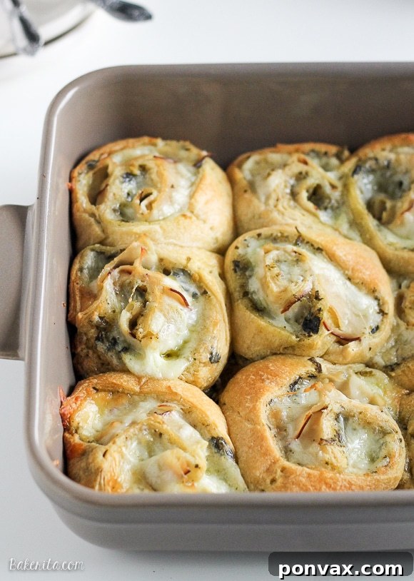 Cheesy Turkey Pesto Pinwheels 6 A hand picking up one of the warm Cheesy Turkey Pesto Rolls from a white serving platter, showing the irresistible melted cheese.